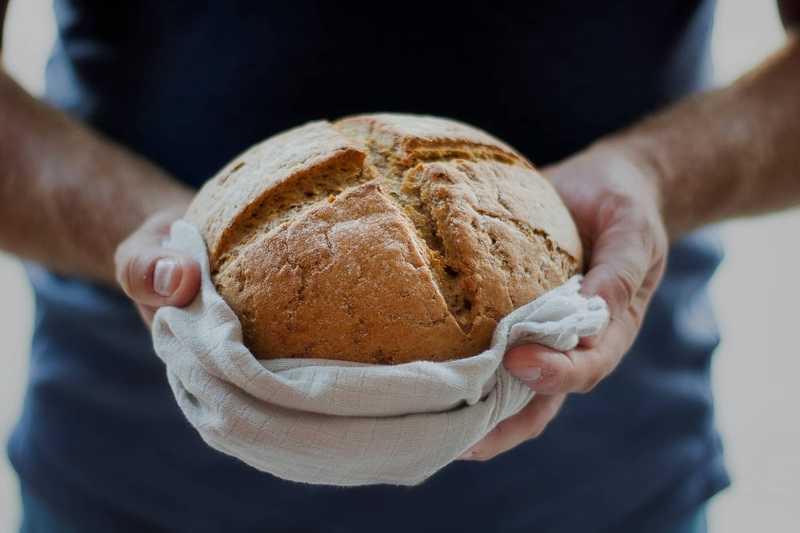 two hands holding out a circular loaf of bread wrapped in a cloth